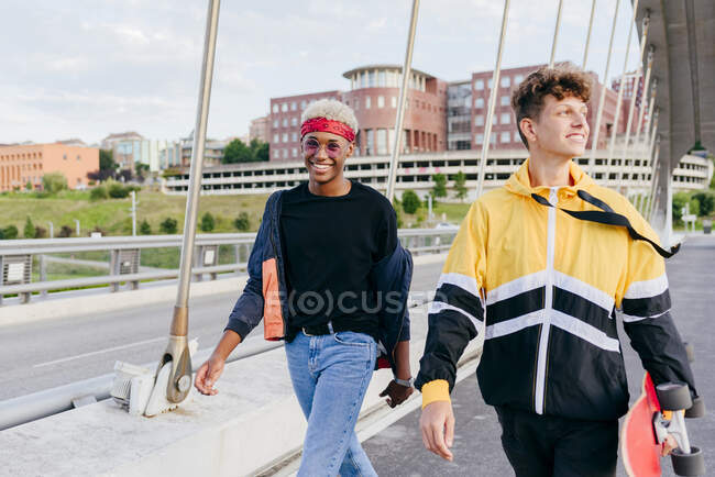 Два симпатичных подростка со скейтбордом идут по мосту — стоковое фото