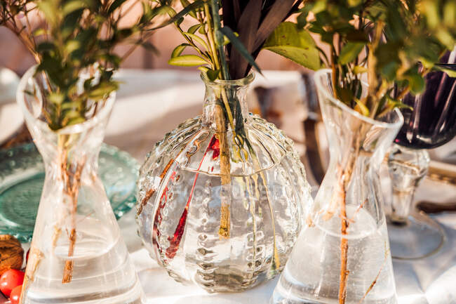 Alto ángulo de jarrones de vidrio transparente con racimos de flores frescas colocadas en la mesa para el evento - foto de stock