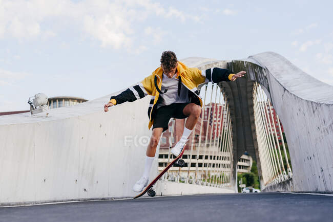 Caucásico adolescente saltando con un monopatín en el medio del puente en la ciudad - foto de stock