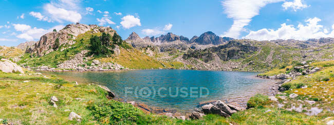 Великолепный пейзаж грубой скалистой горной цепи, окружающей спокойное голубое озеро под ясным голубым небом в солнечный летний день в Пиренеях Каталонии — стоковое фото