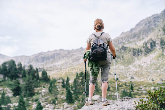 Back view anonymous female hiker in casual clothes with backpack with Nordic walk poles while standing on stony hilltop in mountainous Ruda Valley in Catalan Pyrenees — Stock Photo