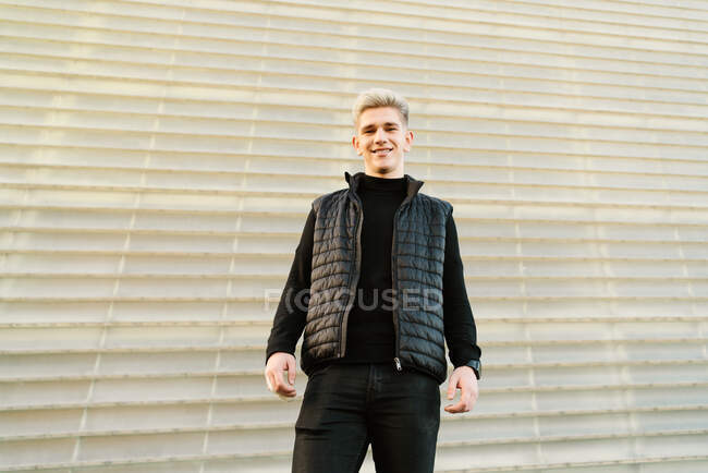 D'en bas jeune homme heureux en tenue tendance debout sur la rue pavée et regardant la caméra le jour ensoleillé — Photo de stock