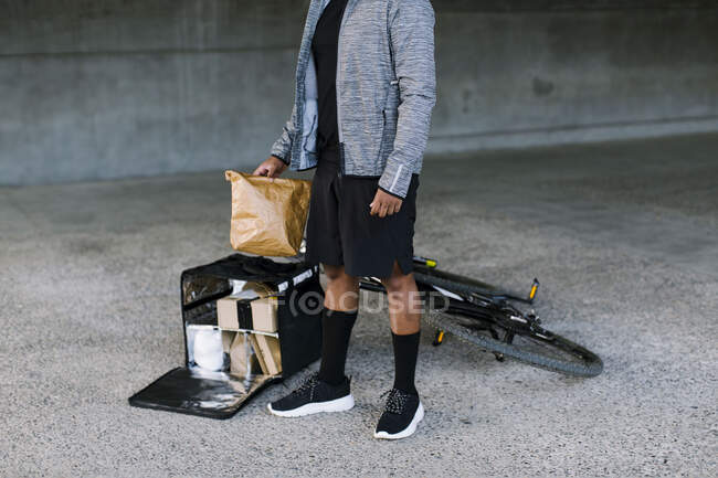 Amerikanischer Auslieferungsfahrer in trendiger Kleidung steht in der Nähe einer Box mit Paketen und Fahrrad und freut sich auf die Stadt — Stockfoto