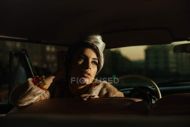 Crop femelle à la mode avec fleur sur le chapeau dans l'automobile tout en regardant loin — Photo de stock