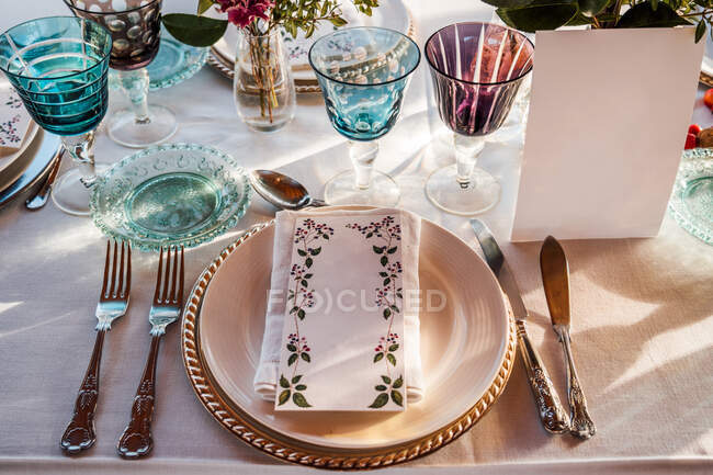 Высокий угол подаваемого праздничного стола с хрустальными стекольными столовыми приборами салфетка на тарелке рядом с букет свежих цветов для свадьбы и меню карты — стоковое фото