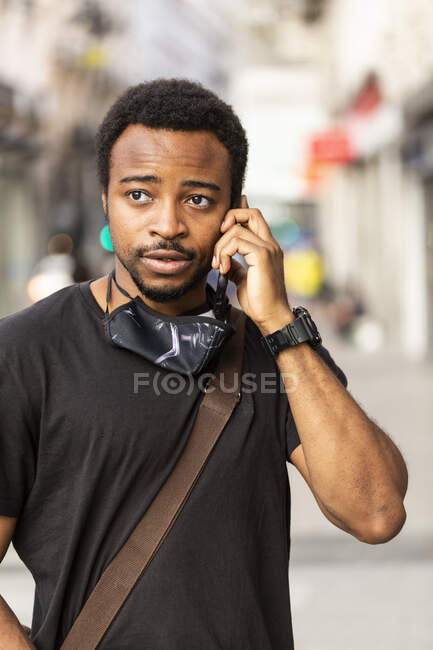 Junger Afroamerikaner in Armbanduhr spricht mit Handy, während er in der Stadt wegschaut — Stockfoto
