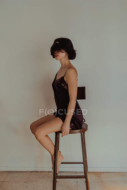 Seitenansicht einer zarten Frau im Nachthemd, die zu Hause auf einem Holzhocker sitzt — Stockfoto
