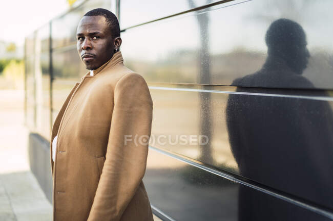 Confident young African American guy in stylish turtleneck sweater and coat standing on street and looking at camera — Stock Photo