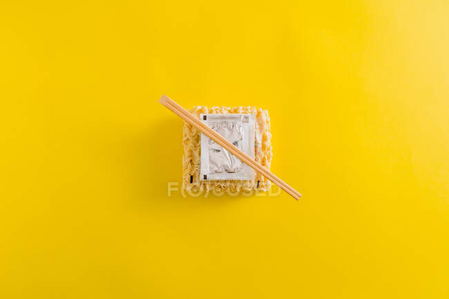 Mise en page des nouilles crues avec des épices ingrédients et bâtonnets dans des emballages en plastique sur fond jaune — Photo de stock