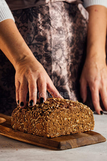 Coltivare anonimo panettiere femminile in possesso di pane con semi di girasole sul tavolo in panetteria — Foto stock
