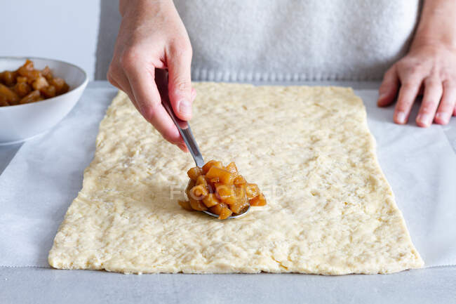 Cultivez une cuisinière anonyme en mettant des tranches de pomme cuites douces sur la pâte tout en préparant une pâtisserie à la maison — Photo de stock