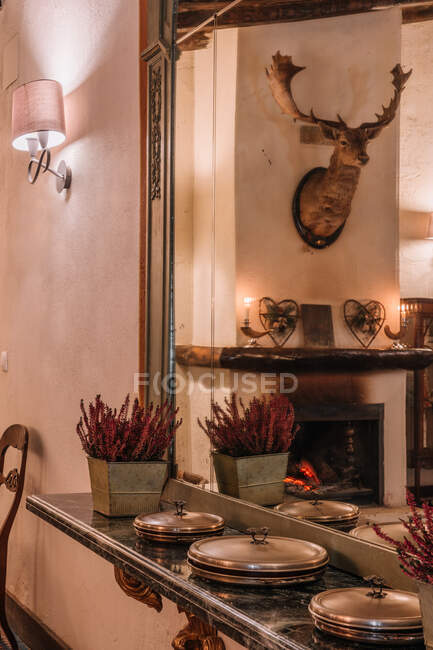 Interior da sala de jantar com placas e flores Calluna na prateleira perto do espelho à noite — Fotografia de Stock