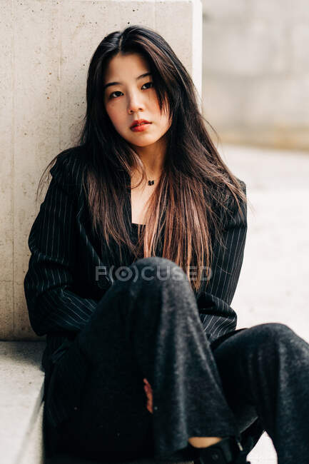 Довге волосся брюнетка азіатська жінка сидить на деяких сходах і дивиться на камеру — стокове фото