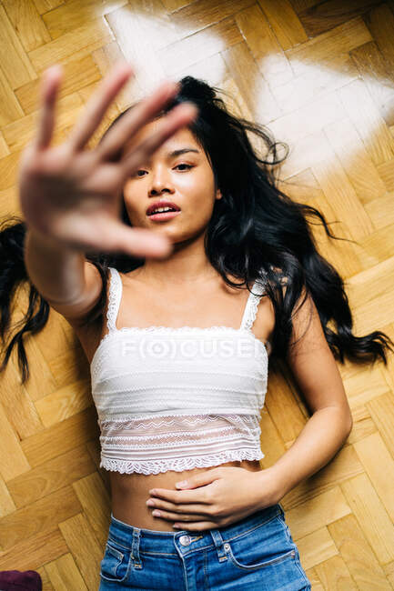 Cabello largo morena asiática mujer tumbada en el suelo en casa y mirando a la cámara - foto de stock