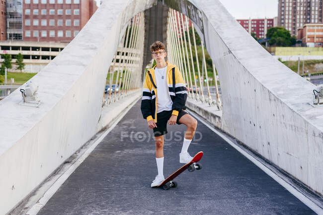 Adolescente caucásica de pie con un monopatín en el medio del puente en la ciudad - foto de stock