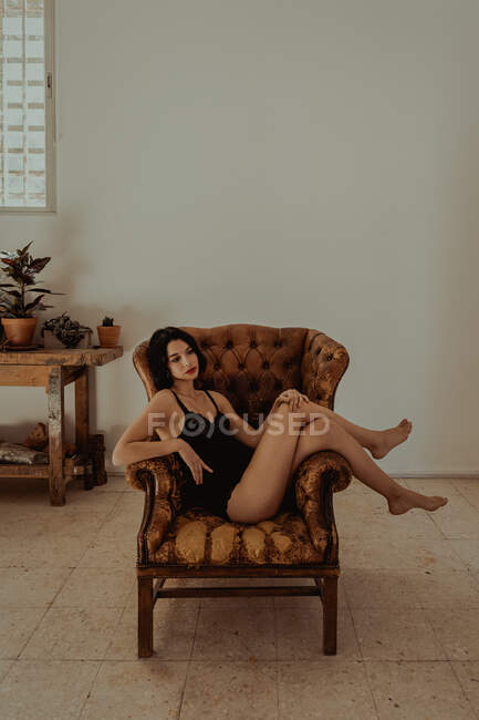 Vista lateral da fêmea pacífica em camisola sentada em poltrona de couro e relaxante — Fotografia de Stock