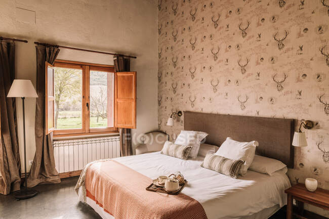 Interior do quarto elegante com cama confortável coberto com coverlet perto da janela decorada com cortinas — Fotografia de Stock
