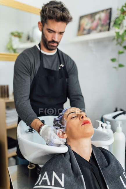 Серйозний молодий чоловік у перукарні, який пере волосся жінки в раковині після стрижки і фарбування в сучасному салоні краси. — стокове фото