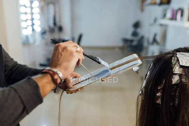 Бічний вид культури сфокусований чоловік майстер об'єднує нитки невпізнаваних жінок-клієнтів перед фарбуванням в техніку балансу — стокове фото