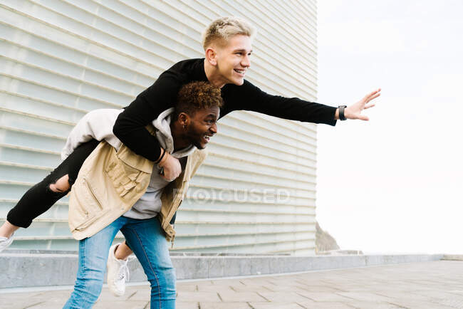From below of cheerful young black boy giving piggyback ride to joyful friend while spending time together in city park — Stock Photo