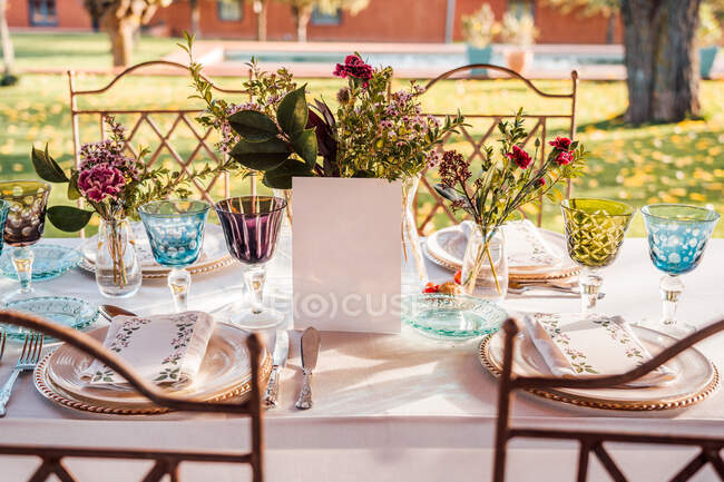 Angle élevé de table de fête servie avec des verres en cristal serviette de coutellerie sur l'assiette près de bouquet de fleurs fraîches pour mariage et carte de menu — Photo de stock
