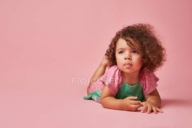 Niño adorable en vestido con el pelo rizado mirando hacia otro lado apoyado con las manos en el suelo - foto de stock