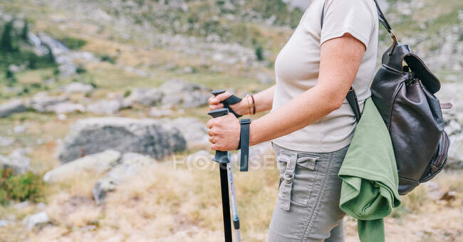 Escursionista anonima ritagliata in abiti casual con zaino con bastoni da nordic walk mentre in piedi su una collina rocciosa nella montagnosa Ruda Valley nei Pirenei Catalani — Foto stock