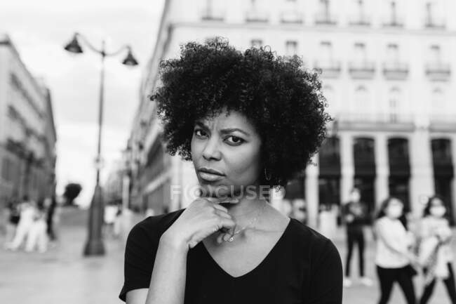 Giovane donna afro-americana riflessiva con acconciatura afro guardando la fotocamera sulla strada della città — Foto stock
