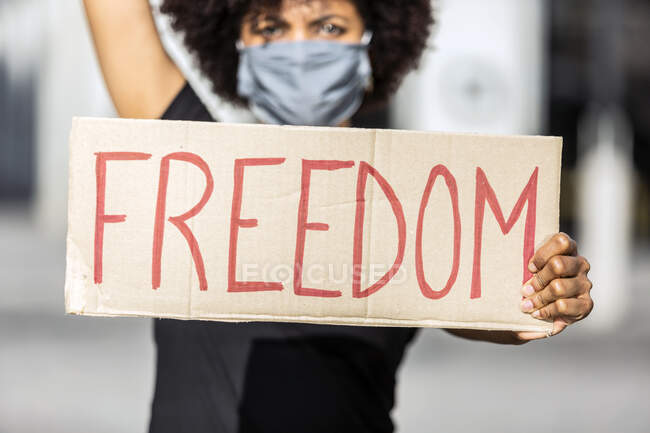 Crop anonymous ethnic female activist in mask showing cardboard placard with Freedom title during BLM demonstration on city street — Stock Photo
