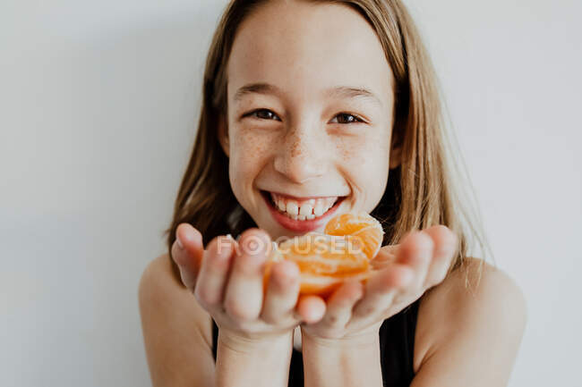 Сеять позитивную девушку с веснушками, улыбающейся и смотрящей в камеру, демонстрируя кусочки свежего здорового мандарина — стоковое фото