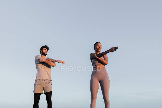 Fit sportswoman with male athlete in sports clothes stretching arms — Stock Photo