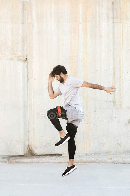 Seitenansicht eines jungen unrasierten männlichen Athleten in Sportbekleidung, der tagsüber beim Training über den Bürgersteig springt — Stockfoto