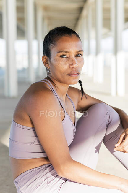 Seitenansicht einer jungen ethnischen Sportlerin in aktiver Kleidung beim Training auf dem Bürgersteig, während sie in die Kamera schaut — Stockfoto