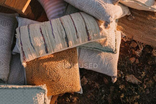 Верхняя стеллаж различных подушек с красочными вязаными наволочками, расположенных на земле в сельской местности под солнечным светом на сельской местности — стоковое фото