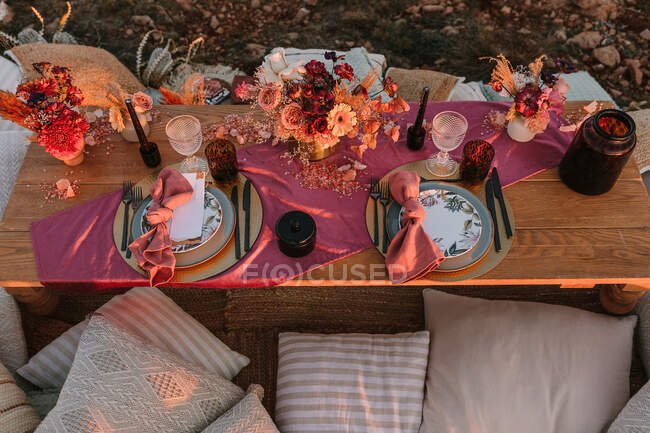 Von oben hölzerne Tischdekoration mit Besteck auf Tellern, serviert auf Tuch neben bunten Blumensträußen mit Weingläsern während der Hochzeitsfeier — Stockfoto