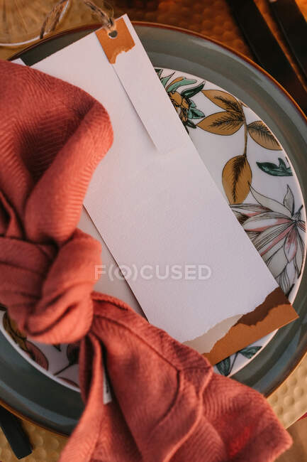 Top view of ornamental plate with colorful napkin with knot and white greeting card placed on table during wedding celebration — Stock Photo