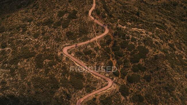 Drone Ansicht der schmalen kurvenreichen ländlichen Straße durch bergiges Land mit grünen Bäumen und Sträuchern in der Natur in der Landschaft — Stockfoto