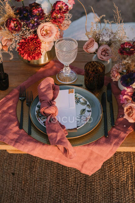 De dessus de table en bois avec couverts sur assiettes servies sur tissu près de bouquets colorés de fleurs avec verres à vin lors de la célébration du mariage — Photo de stock