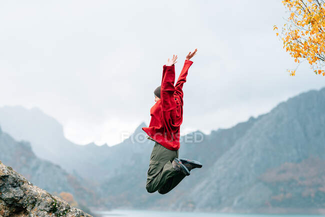 Viajante anônimo de corpo inteiro em roupas quentes pulando com os braços levantados em emoção em terras altas enevoadas no dia de outono — Fotografia de Stock