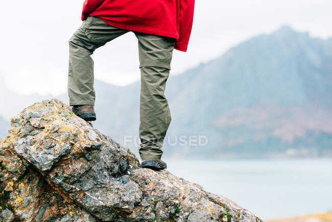 Indietro vista anonimo viaggiatore in abiti caldi in piedi su roccia massiccia e ammirare panoramica catena montuosa che circonda tranquillo lago il giorno d'autunno — Foto stock
