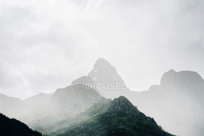 Cenário de picos de cordilheira rochosos ásperos cobertos com névoa densa no dia nublado — Fotografia de Stock