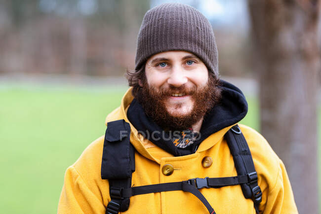 Alegre adulto barbudo viajero masculino de pie sobre la naturaleza a la luz del día - foto de stock