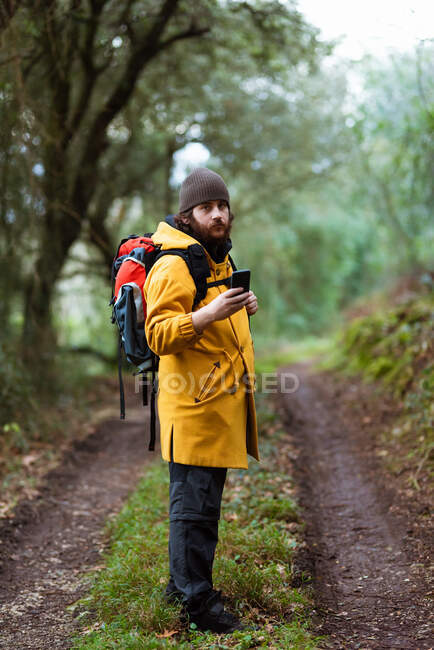 Trekker maschio vista laterale con smartphone di navigazione zaino durante il viaggio alla luce del giorno — Foto stock