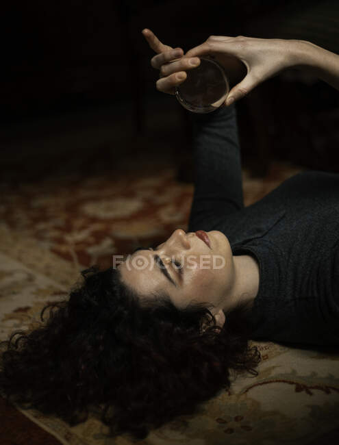 Vue latérale de la femelle détendue avec des cheveux noirs couchés sur le tapis avec boule de cristal transparente dans la chambre avec un design rétro — Photo de stock