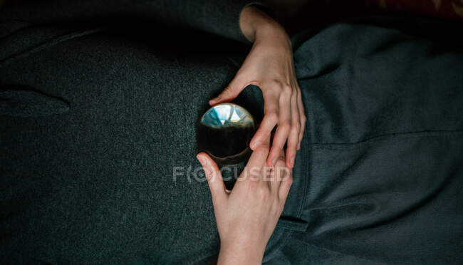 Vista de cerca de la mujer relajada anónima acostada en la alfombra que sostiene la bola de cristal transparente con las manos - foto de stock