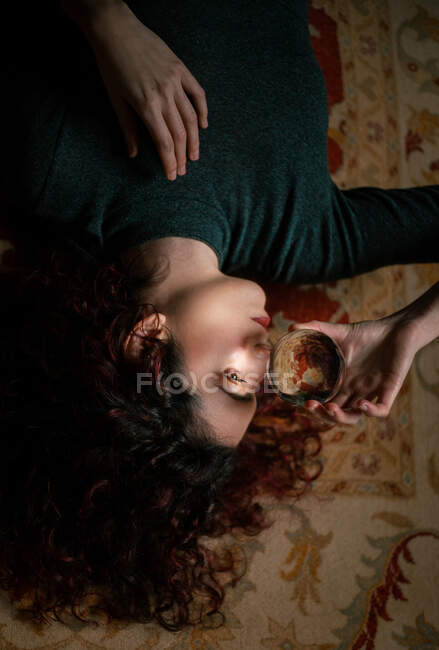 Relaxed female with black hair lying on carpet with transparent crystal ball in room with retro design — Stock Photo