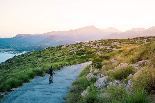 Anonymous female cyclist in casual outfit riding bicycle alone in green highlands with majestic mountains — Stock Photo