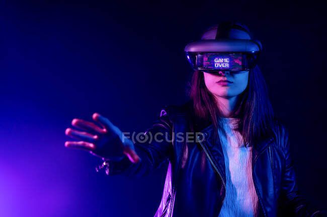 Unrecognizable female with outstretched arm wearing VR headset while exploring virtual reality under blue neon light near wall with projector illumination — Stock Photo