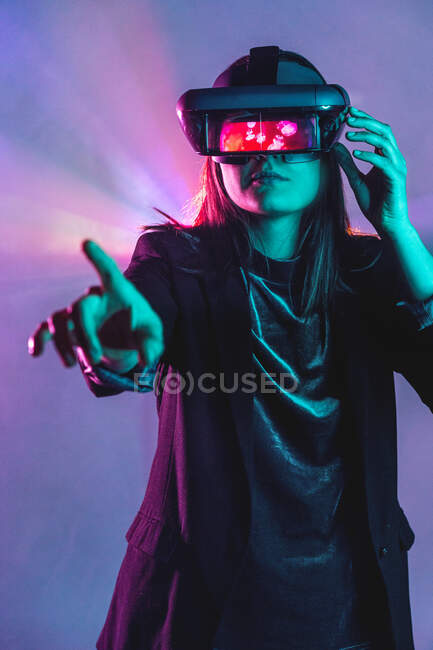Mujer irreconocible con auriculares VR mientras explora la realidad virtual bajo la luz azul de neón - foto de stock