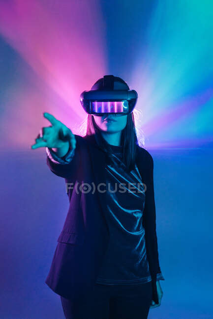 Невпізнавана жінка з витягнутою рукою в гарнітурі VR, вивчаючи віртуальну реальність під блакитним неоновим світлом — стокове фото